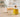 Unlabeled glass bottle of golden chamomile oil beside a handmade soap bar and a few chamomile flowers on a light neutral worktable in bright natural light, with a softly blurred modern workshop background.