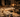 Candle studio workspace at night with multiple white candles in various stages on a wooden table, wax melter, fragrance bottles, and warm ambient lighting