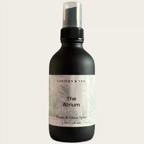 Black room and linen spray bottle labeled 'The Atrium' by Lantern & Veil on a light gray background