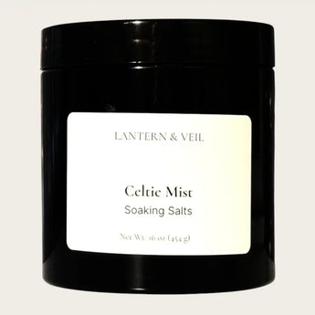 Black container of 'Celtic Mist' soaking salts by Lantern & Veil on a light gray background