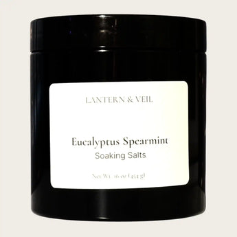 Black container of Eucalyptus Spearmint Soaking Salts with a white label on a light gray background