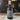 A matte black spray bottle labeled 'Hallowed Ground' stands on a wooden surface in front of a dark shelf with colorful potions and creepy eyeballs.