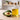 Unlabeled glass bottle of golden avocado oil beside one whole avocado and one halved avocado on a light neutral worktable in bright natural light, with a softly blurred modern workshop background.