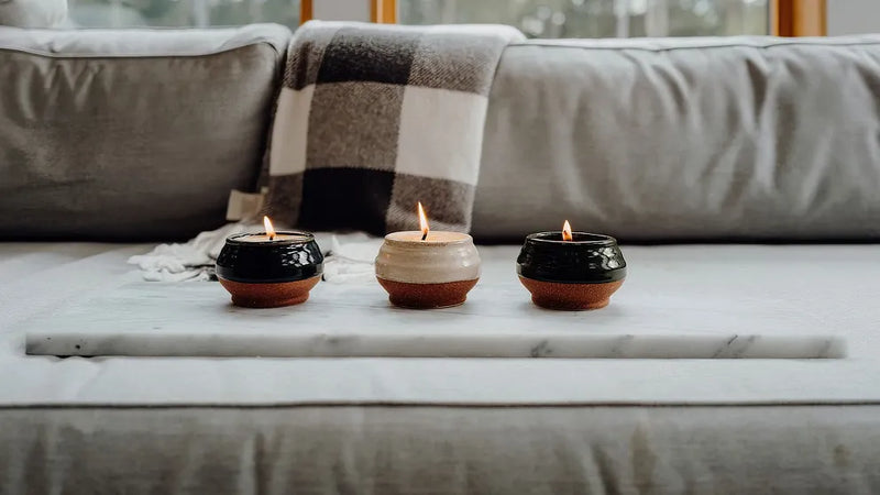 Three small candles burning on a marble tray in a cozy living room setting