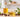 Jojoba oil in a glass bottle and bowl with jojoba seeds and green leaves on a bright, neutral workspace, styled for natural soapmaking ingredients.