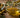 Olive oil being poured into a glass bowl beside olives and olive branches for handmade soap making.