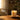 Warm sunlight pours into a cozy living space, illuminating a lit candle on a rustic wooden table beside soft textiles and greenery, creating a calm and inviting atmosphere.