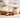Bowl and glass jar filled with creamy shea butter on a light neutral worktable, with a few shea nuts nearby, in bright natural light against a softly blurred modern workshop background.