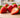 Close-up of several fresh strawberries on a light wooden surface in bright natural light, with the image emphasizing the tiny seeds and texture on the fruit’s surface against a softly blurred background.