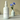 White bottle of 'Aegean Coast' fragrance mist with a vase of blue flowers on a beige background