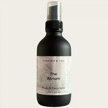 Black room and linen spray bottle labeled 'The Atrium' by Lantern & Veil on a light gray background