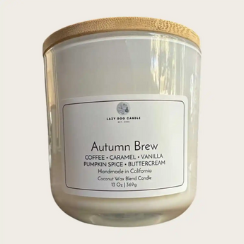 A candle in a white glass jar with a light wood bamboo lid, featuring a white label that reads 'Autumn Brew' 