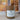 A matte mocha candle jar with a white label reading 'Autumn Mischief'  set against a blurred window background.