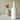 White spray bottle labeled 'Beça Flor' next to a pink flower in a vase on a light surface.