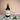 Bottle of 'Bourbon Sunset' room & linen spray with a label on a gray surface with white flowers and green leaves.