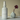 White bottle of 'Crimson Veil' fragrance mist with a small white vase and purple flower on a beige background