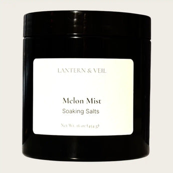 Black container of 'Melon Mist' soaking salts by Lantern & Veil on a beige background