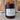 A candle in a matte wine jar with a white label reading 'Midnight Harvest' set on a textured surface in front of a softly blurred fall window background.