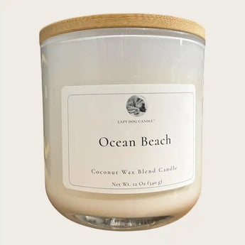 A 12 oz glass jar candle with a light wood bamboo lid, and a white label reading 'Ocean Beach' 