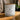 A frosted white glass candle jar with a light wood lid sits on a wooden table. The front label reads 'The Atrium Enchanted Escapes Coconut Wax Blend Candle' 