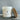 A jar candle labeled 'Tidewater Spa Enchanted Escapes' by Lazy Dog Candle, shown with its wooden lid leaning against the jar on a gray surface against a gray wall.