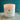 A jar candle labeled 'Tidewater Spa Enchanted Escapes'  sitting on a light wood surface against a teal background.