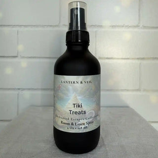 Black spray bottle labeled 'Tiki Treats' by Lantern & Veil on a light gray surface with a white tiled wall background.